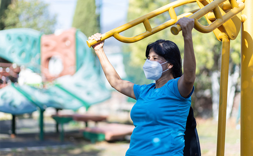 A woman with a face mask using outdoor exercise equipment