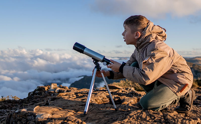 Stock photo of a child on a mountaintop using a telescope.