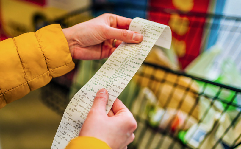 A person’s hands holding a long receipt at the grocery store.