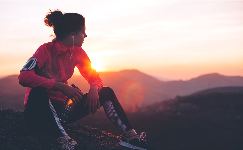 Runner resting and listening to music at sunset